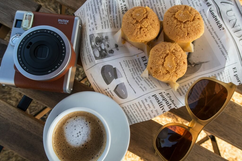 Coffee, cookies, camera, and sunglasses on a table.
